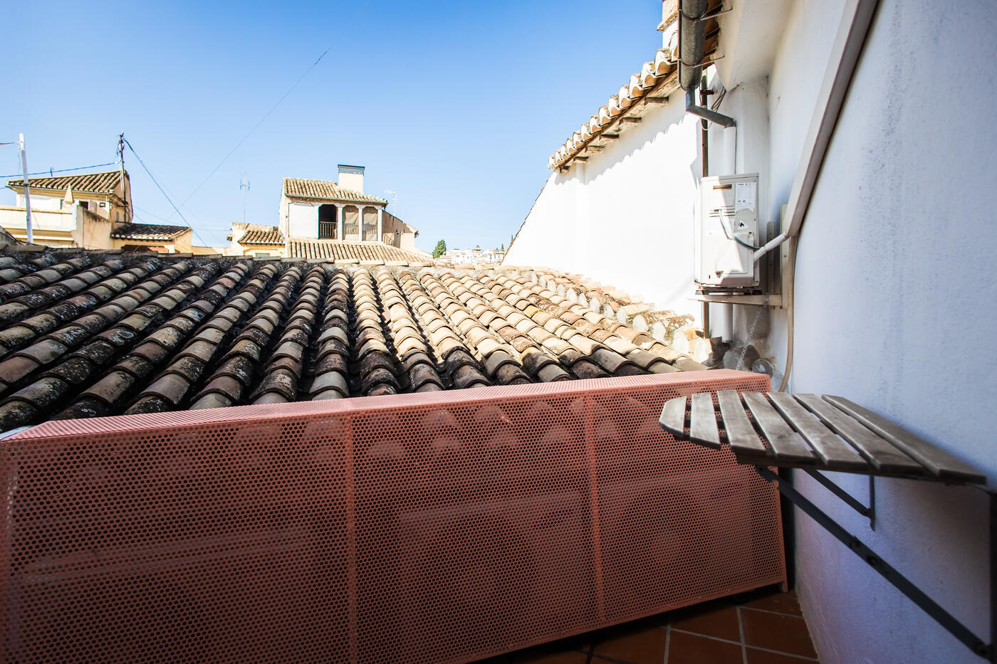 Terraza estrecha de la Suite Mulhacén, con una mesa plegable de madera, asomada a un tejado de teja árabe del casco antiguo.